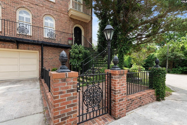 exterior space featuring an attached garage, brick siding, a gate, concrete driveway, and a balcony