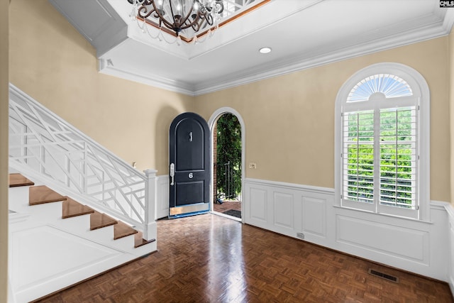 foyer entrance with visible vents, wainscoting, crown molding, and a chandelier
