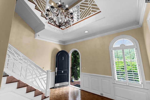 entryway with crown molding, wainscoting, a notable chandelier, and stairway