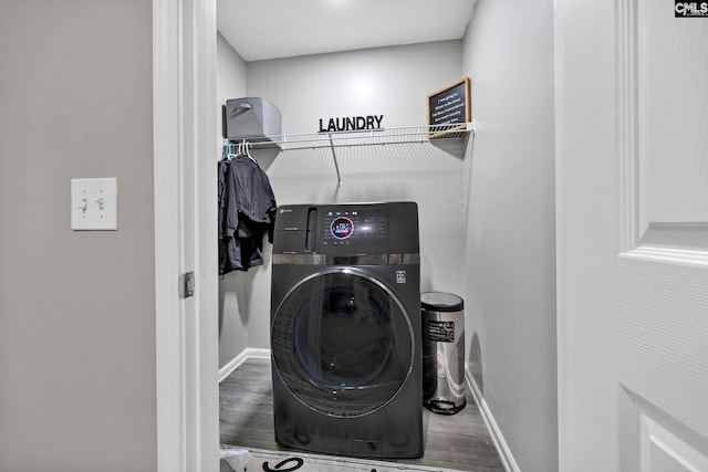 clothes washing area with laundry area, baseboards, washer / dryer, and wood finished floors
