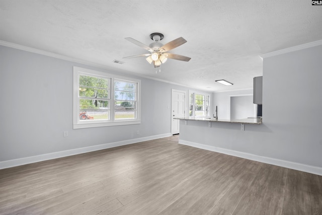 unfurnished living room with baseboards, ceiling fan, ornamental molding, and wood finished floors