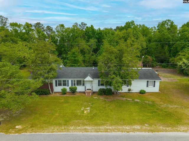view of front of house with a shingled roof, a view of trees, and a front yard