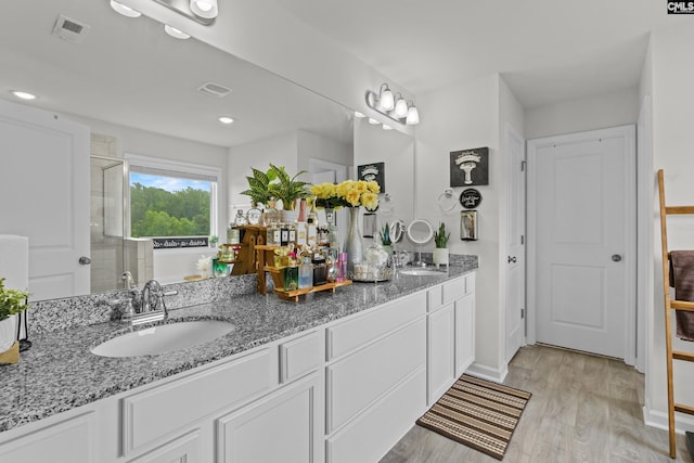 bathroom featuring a sink, double vanity, a shower stall, wood finished floors, and visible vents