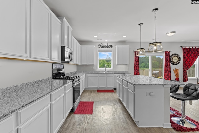 kitchen with white cabinets, appliances with stainless steel finishes, a sink, light wood-style floors, and a center island