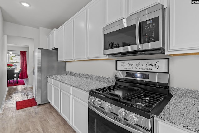 kitchen featuring white cabinetry, light stone countertops, appliances with stainless steel finishes, and light wood finished floors