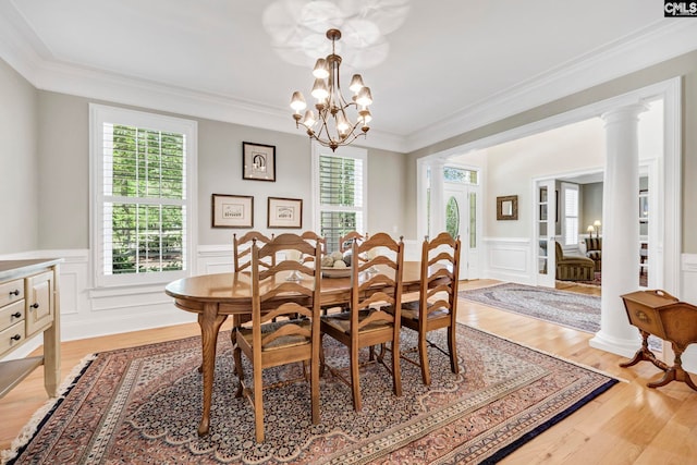 dining space with an inviting chandelier, ornamental molding, a wainscoted wall, and light wood-style floors