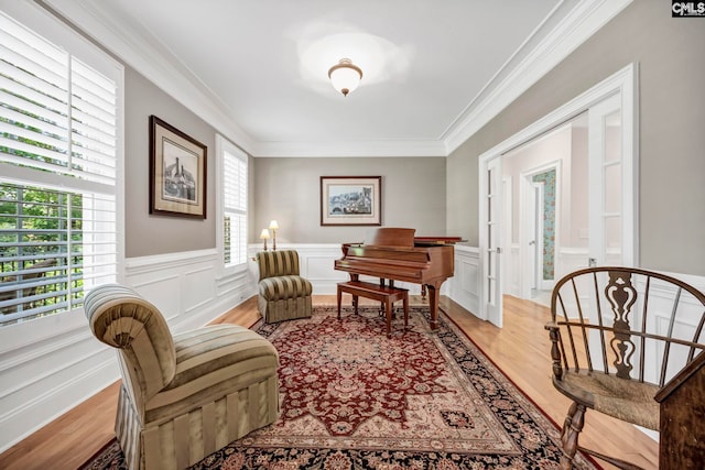 sitting room featuring wainscoting, ornamental molding, light wood-style flooring, and a decorative wall