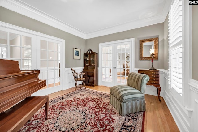 sitting room with crown molding, a decorative wall, wood finished floors, and a wainscoted wall