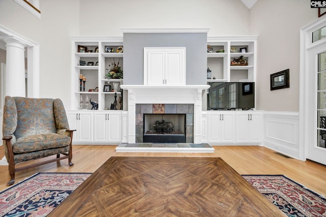 living room featuring light wood-type flooring, a wainscoted wall, and a tile fireplace