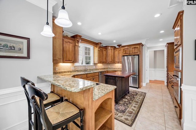 kitchen featuring a peninsula, a decorative wall, a kitchen island, brown cabinets, and appliances with stainless steel finishes
