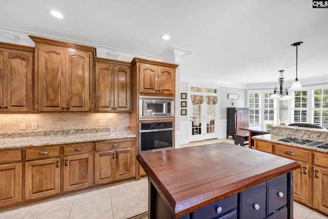 kitchen featuring a kitchen island, crown molding, appliances with stainless steel finishes, hanging light fixtures, and butcher block countertops