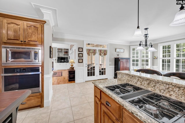 kitchen featuring ornamental molding, brown cabinets, light stone counters, decorative light fixtures, and stainless steel appliances