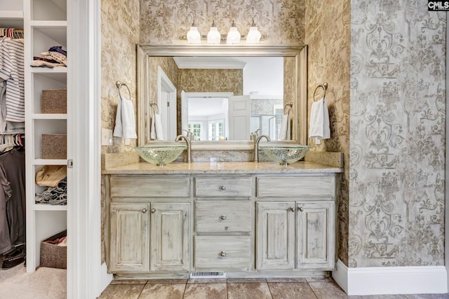 full bathroom featuring double vanity, a sink, a walk in closet, and wallpapered walls