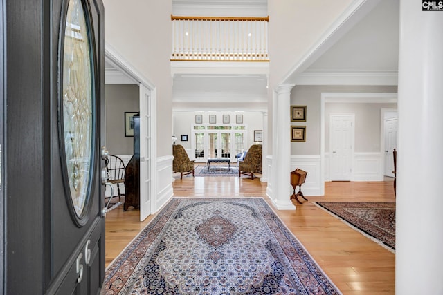 foyer entrance with decorative columns, light wood-type flooring, a wainscoted wall, a high ceiling, and a decorative wall