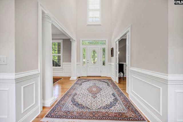 entrance foyer with a decorative wall, ornate columns, light wood finished floors, and a wainscoted wall