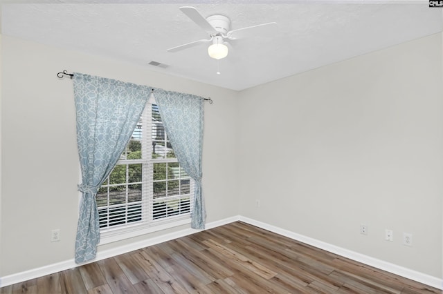 spare room with a ceiling fan, baseboards, visible vents, and wood finished floors