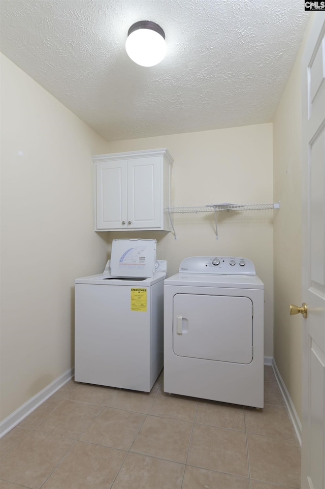 laundry area with cabinet space, separate washer and dryer, a textured ceiling, baseboards, and light tile patterned floors
