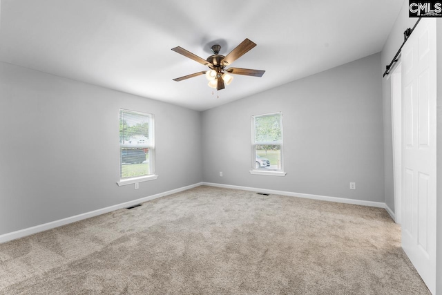 unfurnished bedroom with carpet, visible vents, a barn door, and multiple windows