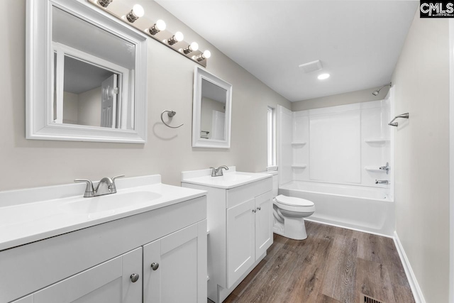 full bath featuring toilet, two vanities, a sink, and wood finished floors