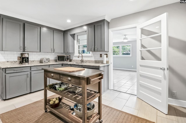 kitchen featuring gray cabinetry, baseboards, stainless steel microwave, and backsplash