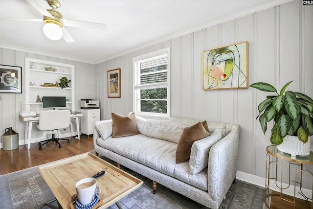 living area featuring crown molding, ceiling fan, wood finished floors, and a decorative wall