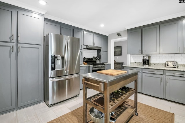 kitchen with decorative backsplash, light stone countertops, gray cabinetry, under cabinet range hood, and stainless steel appliances