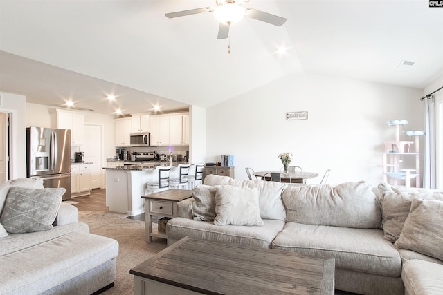 living room featuring ceiling fan, vaulted ceiling, and light colored carpet