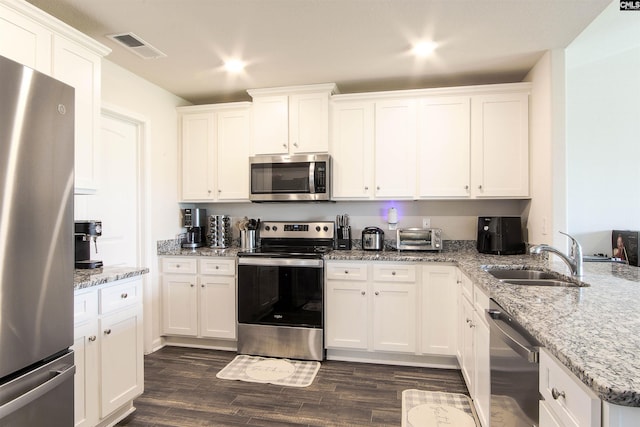 kitchen with appliances with stainless steel finishes, a sink, dark wood finished floors, white cabinetry, and visible vents