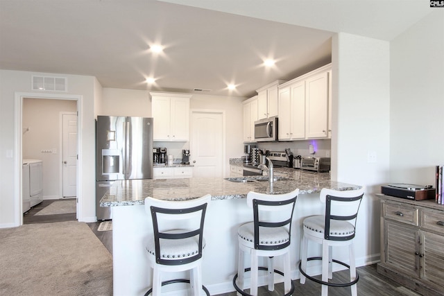 kitchen featuring visible vents, a peninsula, washer and dryer, light stone countertops, and stainless steel appliances