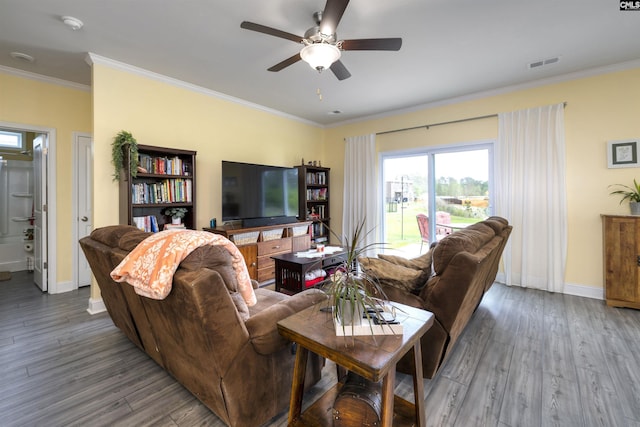 living room with a ceiling fan, baseboards, wood finished floors, visible vents, and ornamental molding