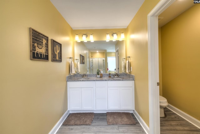 bathroom featuring double vanity, toilet, a sink, and wood finished floors