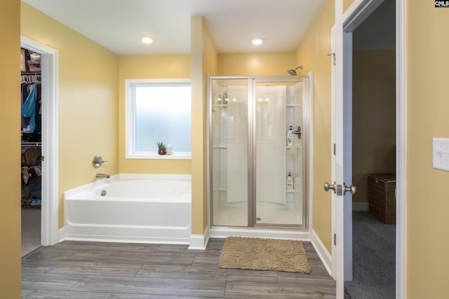 bathroom with a garden tub, a walk in closet, a stall shower, and wood finished floors