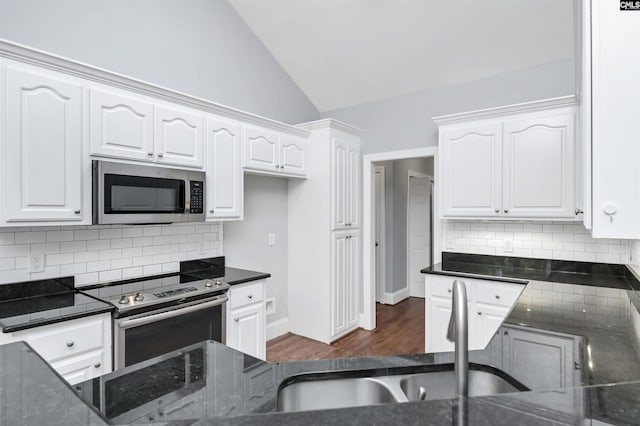 kitchen with dark stone counters, stainless steel appliances, vaulted ceiling, and white cabinetry