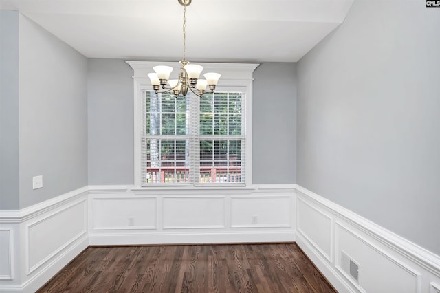 unfurnished dining area featuring visible vents, dark wood-style flooring, a wainscoted wall, and a chandelier