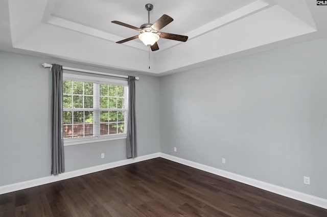 unfurnished room with a ceiling fan, a tray ceiling, dark wood finished floors, and baseboards