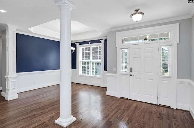 foyer entrance featuring crown molding, a raised ceiling, a wainscoted wall, decorative columns, and dark wood-type flooring