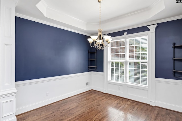 unfurnished dining area featuring decorative columns, wood finished floors, a raised ceiling, a wainscoted wall, and a notable chandelier
