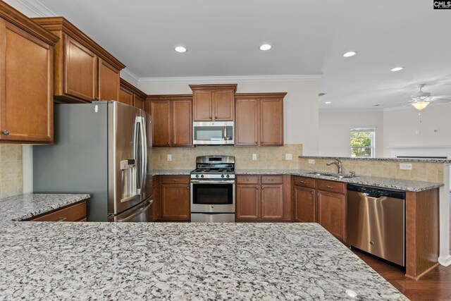 kitchen with brown cabinetry, decorative backsplash, crown molding, a peninsula, and stainless steel appliances