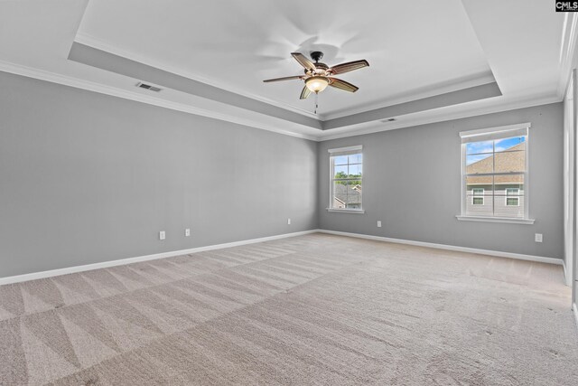 empty room with a ceiling fan, visible vents, a raised ceiling, ornamental molding, and light carpet