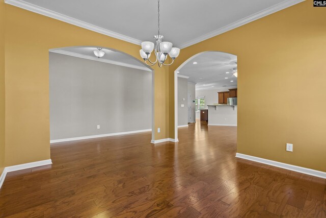 unfurnished dining area featuring crown molding, baseboards, dark wood-style floors, arched walkways, and ceiling fan with notable chandelier
