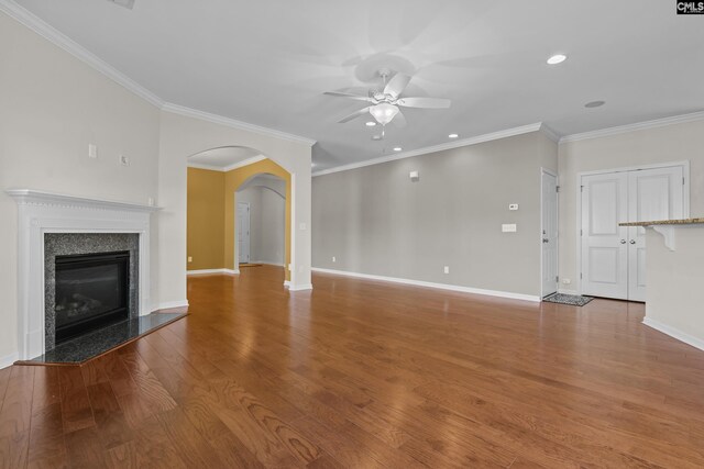 unfurnished living room featuring crown molding, arched walkways, a ceiling fan, and wood finished floors