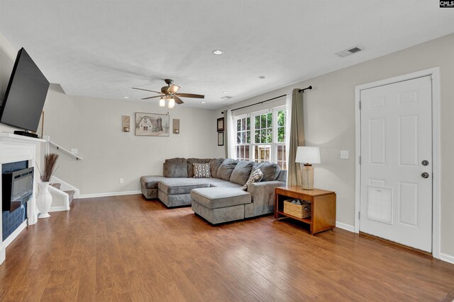 living room featuring a glass covered fireplace, ceiling fan, wood finished floors, and visible vents