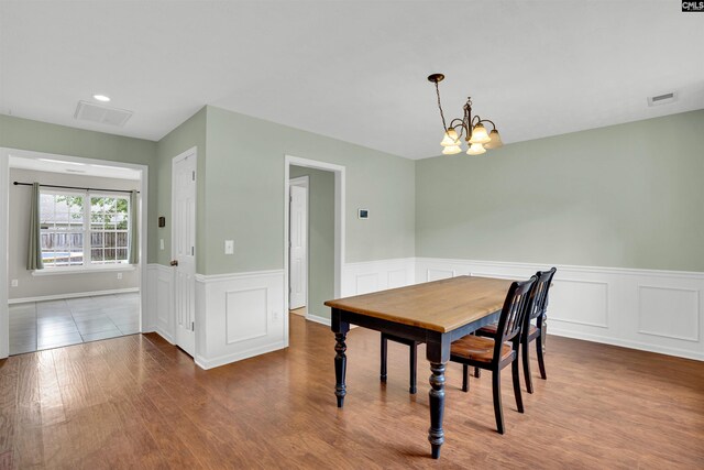 dining room with a wainscoted wall, visible vents, wood finished floors, and a notable chandelier