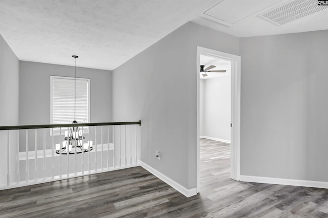 spare room featuring attic access, visible vents, wood finished floors, baseboards, and a chandelier