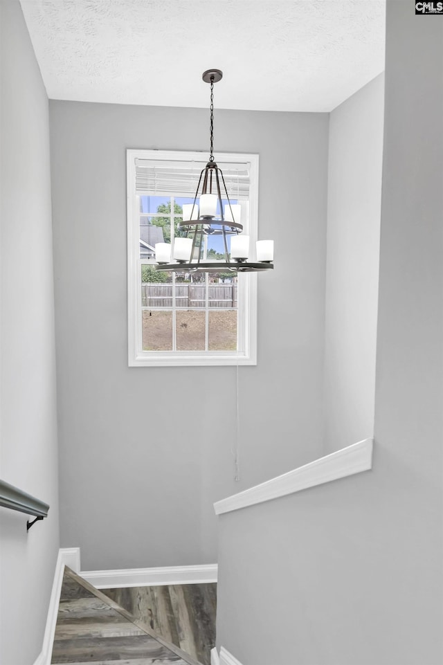 staircase with a textured ceiling, baseboards, a notable chandelier, and wood finished floors