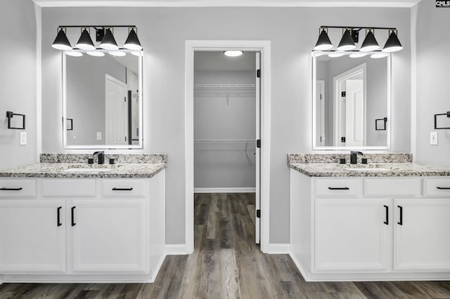 bathroom featuring wood finished floors, a sink, baseboards, and two vanities
