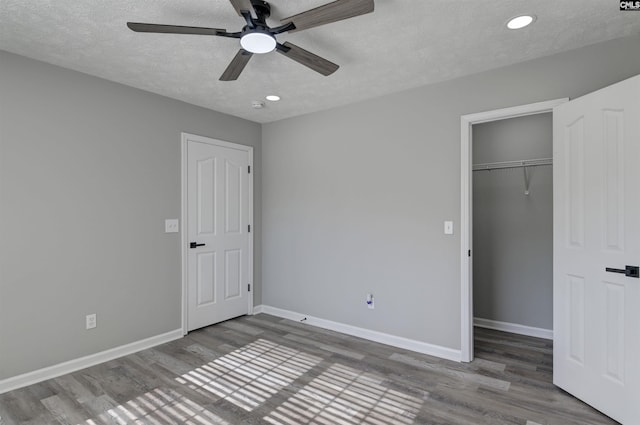 unfurnished bedroom with recessed lighting, baseboards, wood finished floors, and a walk in closet