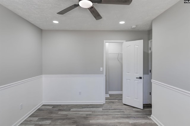 unfurnished bedroom with recessed lighting, a spacious closet, wood finished floors, and a closet