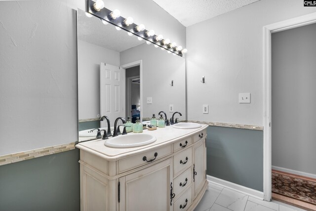 full bathroom with double vanity, a textured ceiling, a sink, and marble finish floor