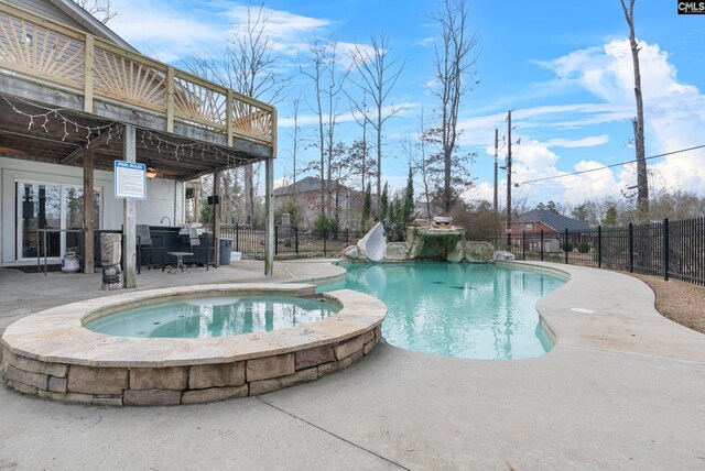 view of swimming pool featuring a pool with connected hot tub, a wooden deck, fence, a patio, and a water slide